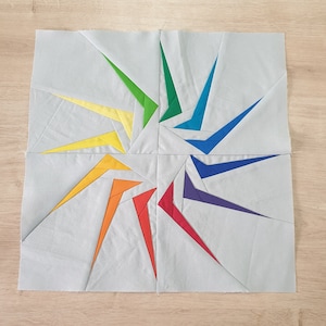 Peut inclure: Un bloc de courtepointe en patchwork avec un motif en étoile éclatante dans les couleurs de l'arc-en-ciel. Le bloc est fait de tissu bleu clair avec différentes pièces de tissu de couleur cousues ensemble pour créer le motif en étoile éclatante.