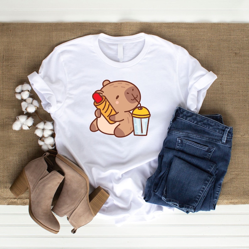May include: White t-shirt with a cartoon illustration of a brown bear holding a hot dog and drinking from a cup with a straw.
