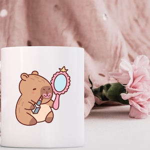 May include: White ceramic mug with a cartoon illustration of a brown capybara wearing lipstick and holding a pink hand mirror with a crown on top.