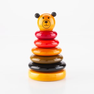 Könnte beinhalten: Ein farbenfrohes Holz-Stapelspielzeug mit einem Bärenkopf oben. Das Spielzeug hat sechs Ringe in den Farben Rot, Orange, Gelb, Grün und Schwarz.
