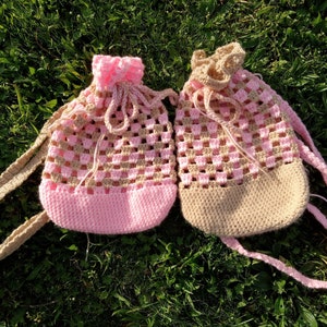 May include: Two crocheted bags with pink and brown yarn. The bags have a drawstring closure and are made with a square stitch pattern.