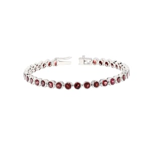 Può includere: Un bracciale in argento con una serie di pietre preziose rotonde di colore rosso intenso. Le pietre sono incastonate vicine, creando una linea continua di colore. Il bracciale ha una chiusura sicura.