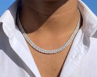 Può includere: Una collana argentata tempestata di diamanti. La collana è in stile cubano, con più file di piccole pietre scintillanti. La collana è indossata su una camicia bianca con colletto, con un cielo blu sullo sfondo.