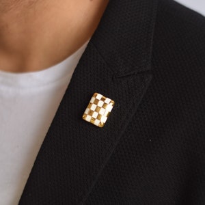 May include: A black blazer with a gold and white checkered lapel pin.