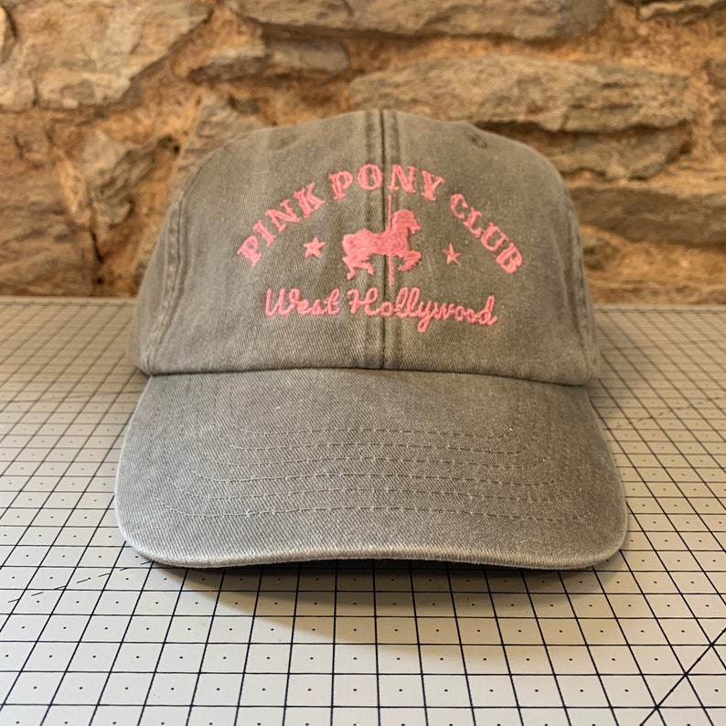May include: A gray baseball cap with a pink embroidered logo that says "Pink Pony Club West Hollywood" and a pink silhouette of a carousel horse.