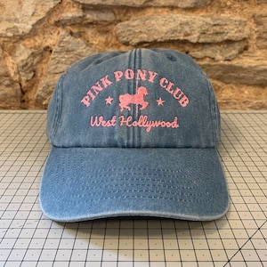 May include: A blue denim baseball cap with an embroidered pink logo that says "Pink Pony Club West Hollywood" with a pink silhouette of a carousel horse.