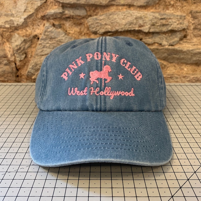 May include: A blue denim baseball cap with an embroidered pink logo that says "Pink Pony Club West Hollywood" with a pink silhouette of a carousel horse.