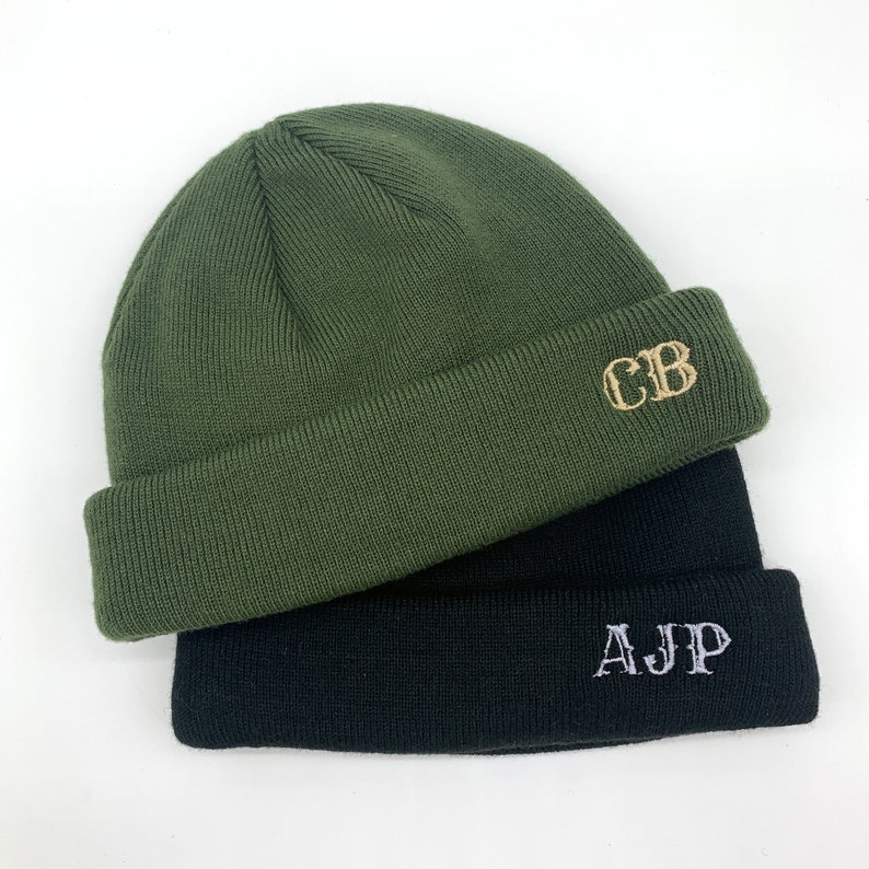 May include: Two knitted beanies, one green with the initials "CB" embroidered in gold thread, and one black with the initials "AJP" embroidered in silver thread.