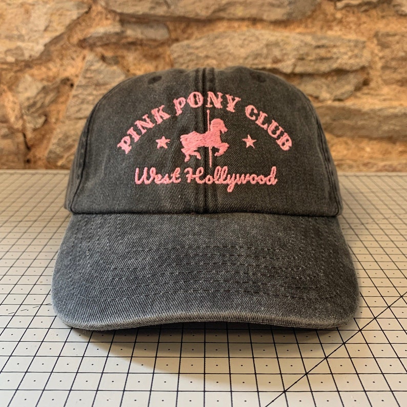 May include: A black denim baseball cap with pink embroidery that reads "Pink Pony Club West Hollywood" and features a pink silhouette of a carousel horse.