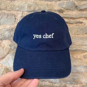 May include: A navy blue baseball cap with white embroidery that reads "yes chef".