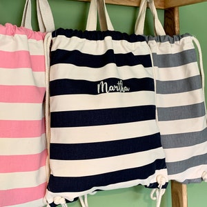 May include: Three striped drawstring bags, one pink and white, one navy blue and white with the name "Martha" embroidered on it, and one grey and white.