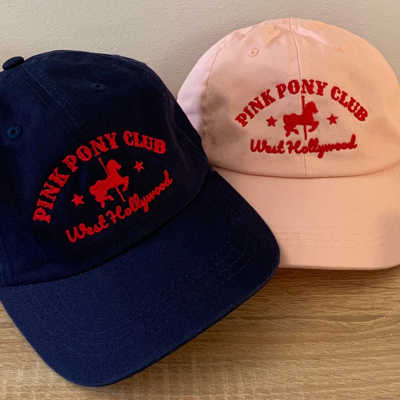 May include: Two baseball caps, one navy blue and one pink, with the same embroidered logo: "Pink Pony Club West Hollywood" in red with a red silhouette of a carousel horse.