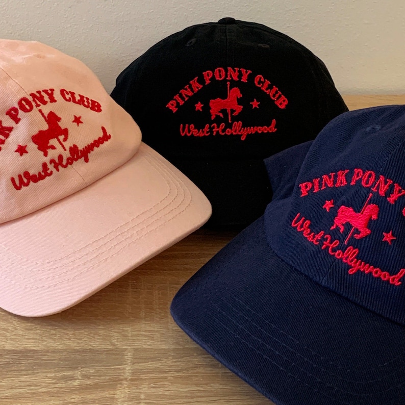 May include: Three baseball caps with the text "Pink Pony Club West Hollywood" embroidered in red on the front. The caps are in pink, black, and navy blue.