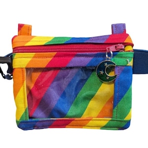 Peut inclure: Une pochette zippée à rayures arc-en-ciel avec une fenêtre en plastique transparent et un charme en forme de croissant de lune. La pochette a une sangle bleue.