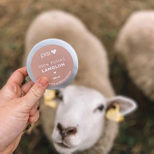 May include: A white metal tin with a pink label that reads "pisi 100% PUHAS LANOLIN 100 ml ETEETÄ JA PESTISSÄÄDIVÄÄ". The tin is being held by a hand in front of a white sheep.