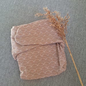 May include: A brown and white patterned cloth nappy with a geometric design of arches. The nappy is folded and lying on a grey textured surface.
