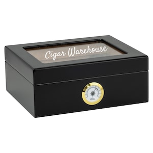 Puede incluir: Humidificador de cigarros de madera negra con tapa de vidrio e higrómetro. El humidificador tiene las palabras "Cigar Warehouse" grabadas en la parte superior.