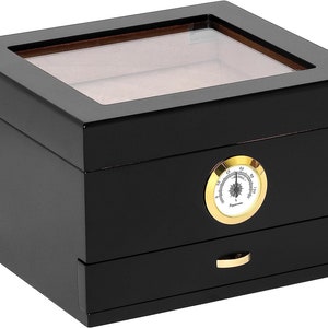 Puede incluir: Humidificador de madera negro con tapa de vidrio e higrómetro incorporado. El humidificador tiene un cajón para guardar los cigarros.