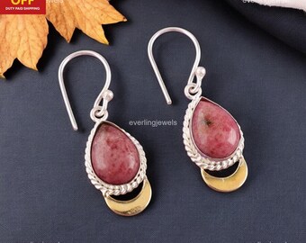May include: A pair of silver earrings featuring teardrop-shaped, pink gemstones. The gemstones are set in a silver frame with a twisted rope design. A gold crescent shape is below the gemstone. The earrings have a hook closure.