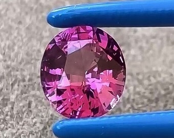 May include: A round, faceted, pink gemstone held by tweezers. The gemstone is a vibrant pink color with a slight purple hue.
