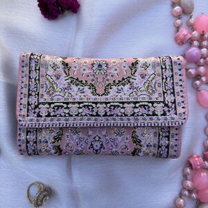 May include: A pink clutch purse with a floral pattern and gold accents. The purse has a flap closure and a small, rectangular shape.