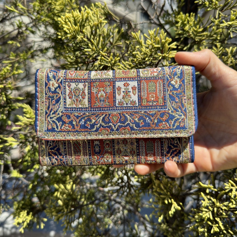 May include: A small, folded wallet with a blue, red, and gold patterned fabric. The fabric has a traditional design with intricate details.