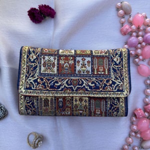 May include: A blue and gold patterned wallet with a traditional rug design. The wallet is closed and has a flap.