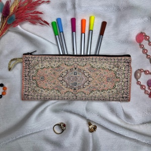 May include: A pink pencil case with a colorful rug design. The case is filled with colorful pens.