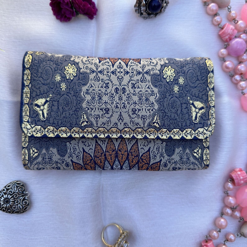 May include: A blue and gold patterned clutch purse with a decorative design. The purse has a flap closure and a gold trim.