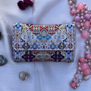 May include: A small, rectangular wallet with a colorful, intricate pattern. The wallet is made of a woven fabric with a blue, red, gold, and white design.