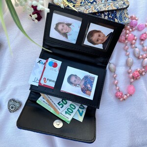 May include: A black leather wallet with a blue and gold patterned exterior. The wallet is open and contains cash, credit cards, and photos.