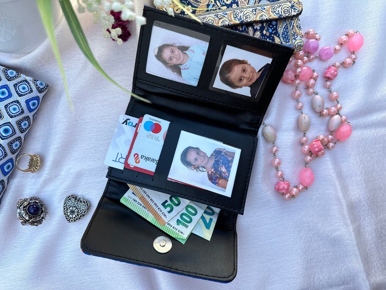 May include: A black leather wallet with a blue and gold patterned exterior. The wallet is open and contains cash, credit cards, and photos.