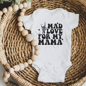 Peut inclure: Combinaison blanche pour bébé avec un texte noir qui dit "Mad Love For My Mama" avec une main de squelette faisant le signe rock and roll.
