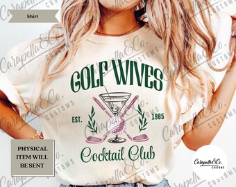 May include: A white t-shirt with a green and white design that says "Golf Wives Cocktail Club" with a martini glass and golf clubs. The text also says "Est. 1985".