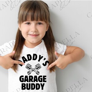 May include: A white t-shirt with black text that reads "Daddy's Garage Buddy" with a graphic of two crossed wrenches.