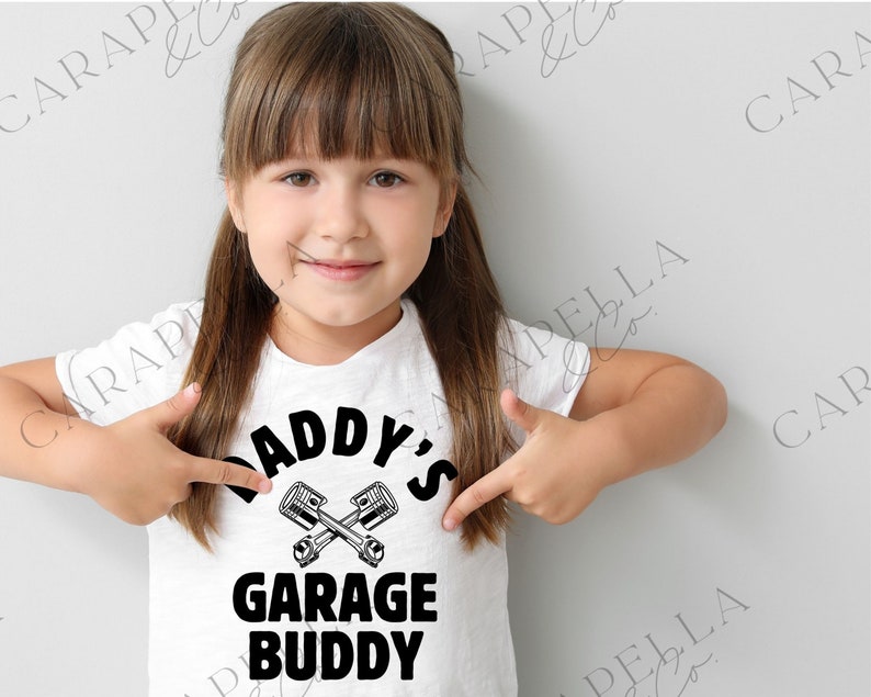 May include: A white t-shirt with black text that reads "Daddy's Garage Buddy" with a graphic of two crossed wrenches.