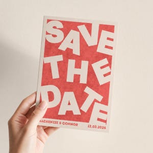 May include: A rectangular invitation card with the words "SAVE THE DATE" in large, white, stylized letters against a red background. The names "Mackenzie & Connor" and the date "12.03.2026" are printed at the bottom.