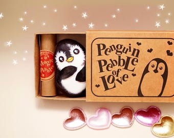 May include: A hand-painted penguin pebble inside a cardboard box labeled "Penguin Pebble of Love." The penguin is black and white with a yellow beak. A scroll and heart-shaped embellishments are also included.