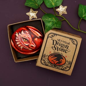 May include: A small, hand-painted stone with a red dragon design. The stone is in a small, brown box with the words "Mystical Dragon Stone" and "Blazing Fire" printed on it.