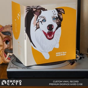 Op de afbeelding: Een custom vinyl record met een gele en witte hoes met een cartoon illustratie van een hond met blauwe ogen. De tekst "NOBU'S lieve kinderliedjes" staat op de hoes. De plaat ligt op een draaitafel.