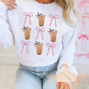 May include: White sweatshirt with a repeated pattern of pink bows and iced coffee cups with straws.