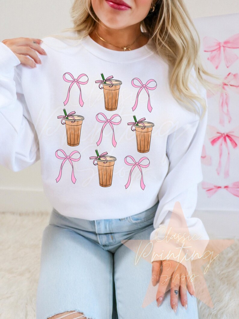 May include: White sweatshirt with a repeated pattern of pink bows and iced coffee cups with straws.