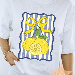 May include: A light gray t-shirt featuring a graphic of two lemons, a lemon slice, and a yellow bow on a blue and white striped background. The text "Classic Printing Shop" is visible in the lower right corner.