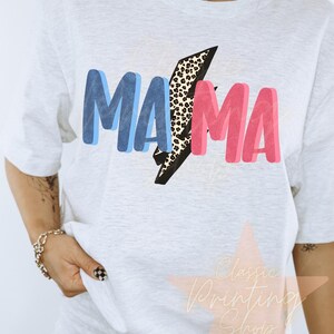May include: White t-shirt with a blue and pink "MAMA" graphic with a leopard print lightning bolt in the middle.