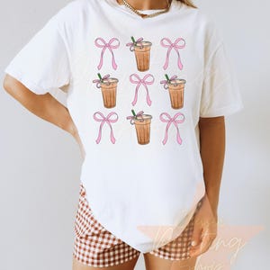 May include: White t-shirt with a pattern of iced coffee drinks with pink bows.