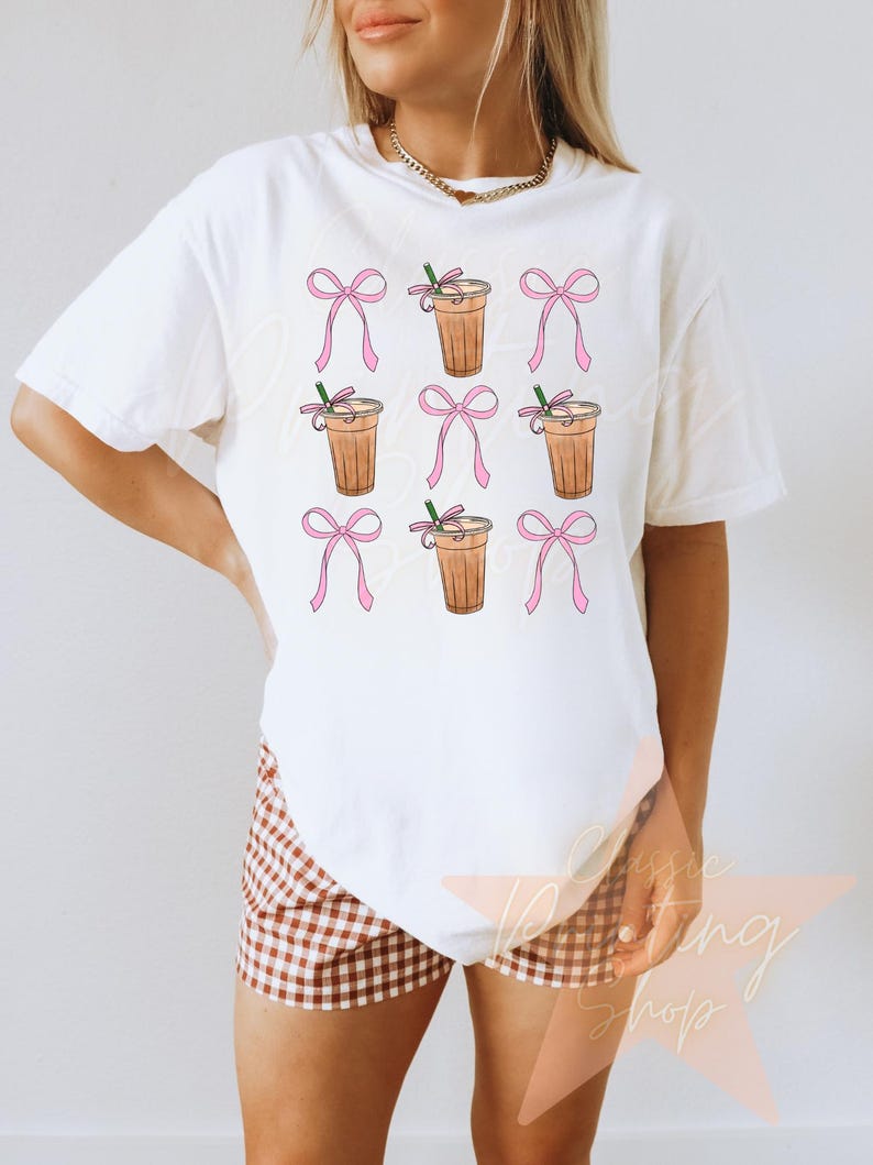 May include: White t-shirt with a pattern of iced coffee drinks with pink bows.