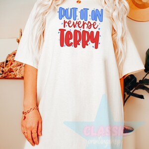 May include: White oversized t-shirt with the text "PUT IT IN REVERSE TERRY" in red and blue lettering with white stars.