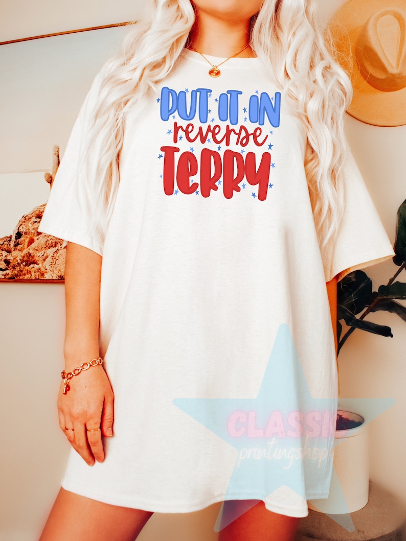 May include: White oversized t-shirt with the text "PUT IT IN REVERSE TERRY" in red and blue lettering with white stars.
