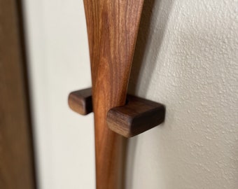 May include: Close-up of a wooden paddle with two wooden brackets attached to the wall. The paddle is a rich brown color and has a smooth finish.