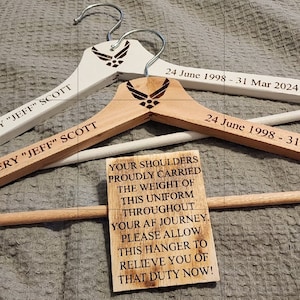 May include: Two wooden hangers with the text "JEFFERY "JEFF" SCOTT" and the dates "24 June 1998 - 31 Mar 2024". A small wooden sign reads "YOUR SHOULDERS PROUDLY CARRIED THE WEIGHT OF THIS UNIFORM THROUGHOUT YOUR AF JOURNEY. PLEASE ALLOW THIS HANGER TO RELIEVE YOU OF THAT DUTY NOW!"